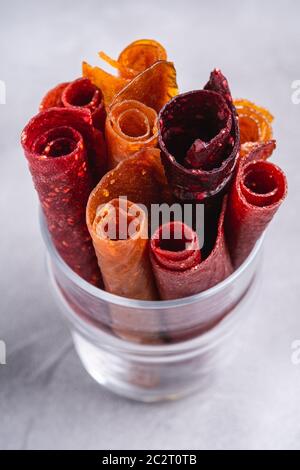 Pastille de fruits dans une tasse de verre sur fond de béton de pierre. Nourriture roulait sans sucre biologique à base de framboise, fraise, pêche et pomme. Maison végétalienne Banque D'Images