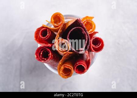 Pastille de fruits dans une tasse de verre sur fond de béton de pierre. Nourriture roulait sans sucre biologique à base de framboise, fraise, pêche et pomme. Maison végétalienne Banque D'Images