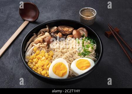 Rampe. Nouilles soba avec œufs, champignons et légumes, saké, cuillère en bois traditionnelle et baguettes sur un backgro noir Banque D'Images