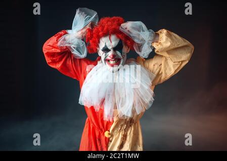 Scary clown sanglant larmes ses cheveux, secousse de colère. Homme avec un miroir en costume de carnaval, crazy maniac Banque D'Images