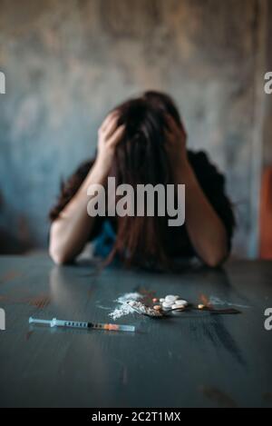 Femme junkie assis à la table avec des médicaments et une seringue, grunge chambre intérieur sur fond. Concept de toxicomanie, les personnes dépendantes Banque D'Images