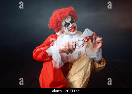 Scary clown sanglant avec un défaut à la recherche de son couteau. Avec l'homme en costume maquillage carnaval, mad maniac Banque D'Images
