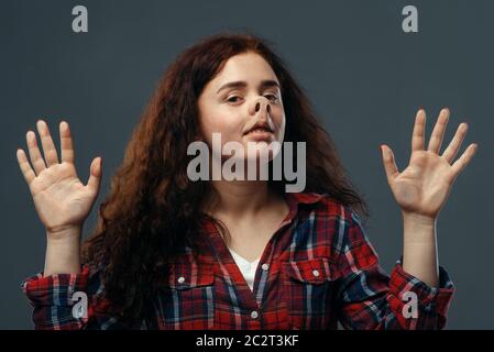 Visage drôle de jeune femme écrasé sur verre transparent. Femme avec une grimace pressée debout à la vitrine, humour, regarder mal à l'aise Banque D'Images