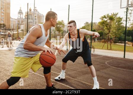 Deux joueurs de basket-ball jouent à un match intense sur un terrain extérieur. Les athlètes masculins de sport jouent au jeu sur l'entraînement de streetball Banque D'Images