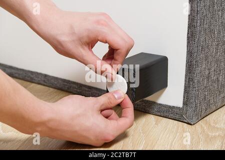 L'homme colle le coussin de soin du sol aux pieds en bois du lit. Couvre-coussin en feutre antidérapant à poser sur la jambe de meuble en bois. Banque D'Images