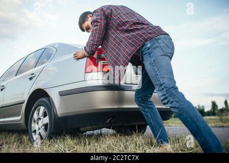 Man pushing casse voiture, vue de côté. Véhicule avec trounble sur route au jour d'été Banque D'Images