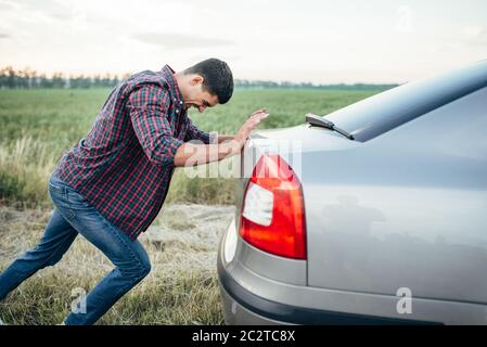 Man pushing casse voiture, vue de côté. Véhicule avec trounble sur route au jour d'été Banque D'Images