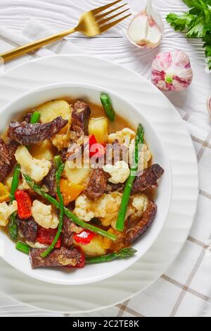 Gros plan de l'été Beef Strip de pommes de terre neuves, asperges et chou-fleur dans un bol blanc sur une table en bois, cuisine américaine, vue verticale fr Banque D'Images