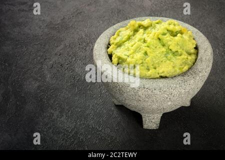 Le guacamole dans un molcajete, avocat mexicain sauce trempette dans le mortier traditionnel en pierre, sur un fond noir avec copie espace Banque D'Images