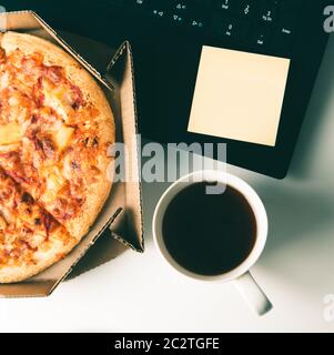 Pizza dans une boîte, tasse de café, ordinateur portable et étiquette vide avec espace pour les copies sur le bureau. Concept de livraison de nourriture ou de pizza et pause le jour ouvrable. Banque D'Images