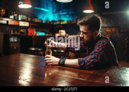 Triste homme assis au bar comptoir et ouvre la bouteille avec de l'alcool des boissons. Personne de sexe masculin dans la pub, l'alcoolisme Banque D'Images