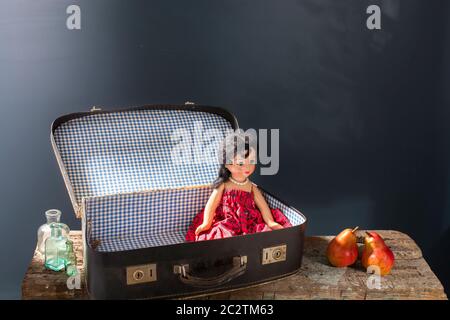 Une vieille poupée dans une valise vintage avec de petites bouteilles sur fond bleu, deux poires sur une surface en bois ruiné du banc. Copier l'espace Banque D'Images