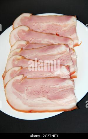 Tranché de viande fumée sur une assiette blanche. Fines tranches de bacon. Assiette de fines tranches de jambon Banque D'Images
