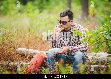 Homme affamé, manger. Sandwich à l'extérieur. Sandwich randonneur en forêt. repas de grignotage pour les touristes. Le randonneur prend une pause avec tim Banque D'Images