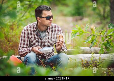 Homme affamé, manger. Sandwich à l'extérieur. Sandwich randonneur en forêt. repas de grignotage pour les touristes. Le randonneur prend une pause avec tim Banque D'Images