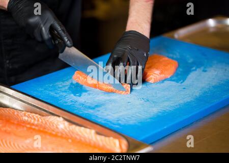 La cuisine à thème est une profession de cuisine. Gros plan sur la main d'un homme caucasien dans une cuisine de restaurant préparant des filets de poisson rouge Banque D'Images