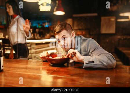 Couple en querelle, homme mange au comptoir du bar, relation amoureuse, dîner avec vin rouge et coller. Amoureux au pub, mari et femme en boite Banque D'Images