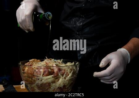 Le chef verse de la viande sur une assiette avec de l'huile d'olive sur fond noir. Marinade de porc avec pommes de terre râpées et oignons gros plan. Banque D'Images