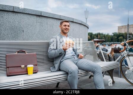 Homme d'affaires avec vélo mange déjeuner sur le banc à l'immeuble de bureaux dans le centre-ville. Personne d'affaires en transport écologique dans la rue de la ville, style urbain Banque D'Images