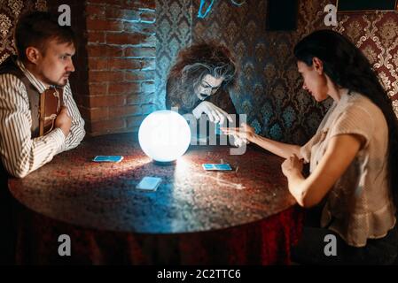 Femme foreteller deviner à la main sur une boule de cristal, la sorcellerie. Sorcière effrayante lit un charme magique, jeune femme sur seance spirituelle Banque D'Images