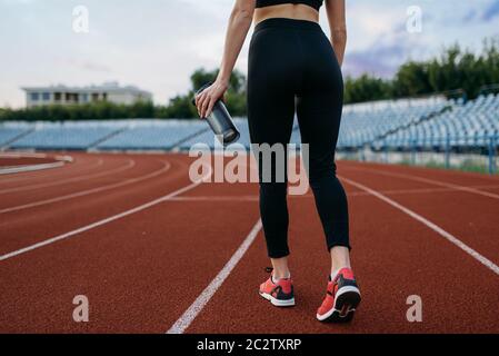 Femme coureur de vêtements de sport, vue arrière, entraînement au stade. Femme qui fait de l'exercice d'étirement avant de courir sur une arène extérieure Banque D'Images