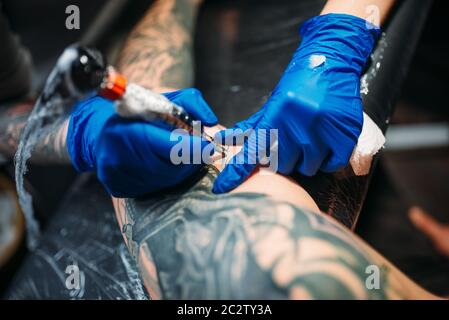 Tatoueur tatouage féminin fait par la machine sur l'épaule masculine. Dans le salon de tatouage professionnel Banque D'Images