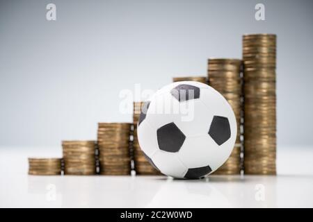 Ballon de soccer en face de piles de pièces d'or sur fond gris blanc 24 Contre Banque D'Images