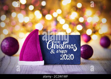 Wth Sighn Calligraphie anglaise Joyeux Noël et une Bonne 2020. Bal de noël ornement violet With Santa Hat. Des lumières scintillantes Background Banque D'Images