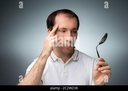 Portrait d'un homme à l'aide de pouvoirs télékinésiques Holding Cuillère en acier inoxydable à l'arrière-plan gris Banque D'Images