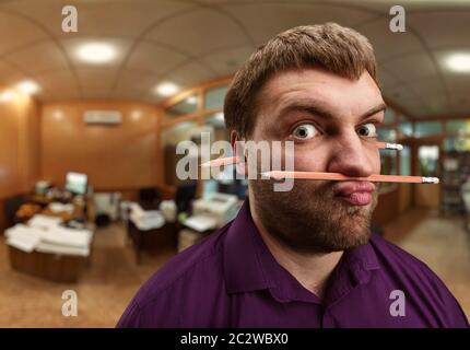 Homme barbu étrange détient avec son nez et crayon lèvres et une plus de crayon dans ses oreilles Banque D'Images
