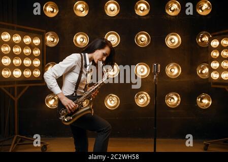 Le saxophoniste féminin joue le saxophone sur la scène avec des spots. Un artiste de jazz jouant sur scène Banque D'Images