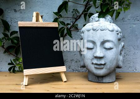 petit tableau noir avec tête de bouddha grise sur table en bois Banque D'Images