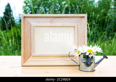 cadre photo en bois sur table avec arrosoir miniature et marguerites en plein air dans la nature Banque D'Images