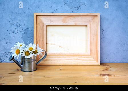 cadre photo en bois sur table avec arrosoir miniature et marguerites sur fond bleu Banque D'Images