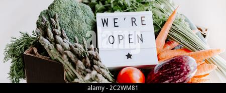 Verrouillage de fin de quarantaine. Visionneuse avec message de bienvenue, nous sommes ouverts et boîte de légumes frais. Accueillir les clients de l'épicerie après c Banque D'Images