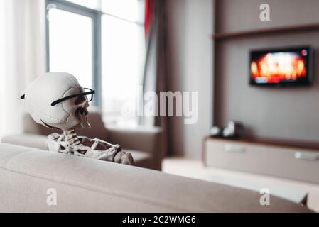 Squelette en lunettes est assis sur le canapé et regarder la télévision, vue de dos, fenêtre sur l'arrière-plan. Drôle Banque D'Images