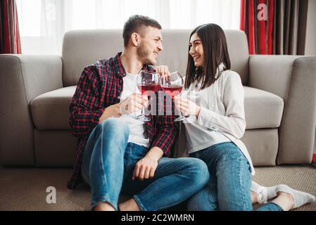 Love couple assis sur le sol contre la table, montres de film et de boissons vin rouge de grands verres, fenêtre et un salon intérieur sur l'arrière-plan. Rom Banque D'Images