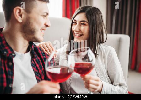 Love couple assis sur le sol contre la table, montres de film et de boissons vin rouge de grands verres, fenêtre et un salon intérieur sur l'arrière-plan. Rom Banque D'Images