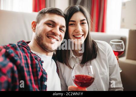 Love couple assis sur le sol contre la table, montres de film et de boissons vin rouge de grands verres, fenêtre et un salon intérieur sur l'arrière-plan. Rom Banque D'Images