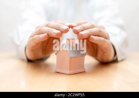 Assurance de biens. Maison miniature couverte par les mains Banque D'Images