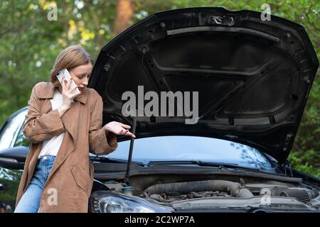 Une femme sans défense, chauffeur appelant pour obtenir de l'aide ou de l'aide, qui a regardé une voiture en panne, s'est arrêtée au bord de la route. Ne comprend pas ce qui s'est passé. Banque D'Images