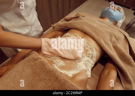 Crème à frotter pour femme au ventre de jeune femme mince dans une serviette, massage professionnel. Massage et relaxation, soins du corps et de la peau. Attrayant l Banque D'Images