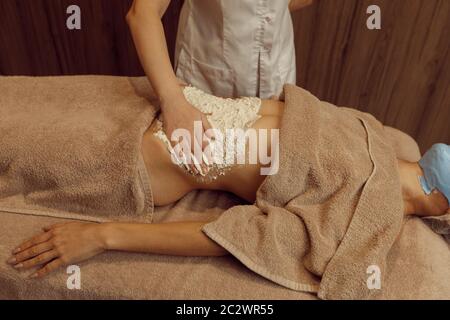 Crème à frotter pour femme au ventre de jeune femme mince dans une serviette, massage professionnel. Massage et relaxation, soins du corps et de la peau. Attrayant l Banque D'Images