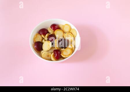 Bol blanc avec petite crêpe aux céréales et cerise sucrée sur fond rose. Copier l'espace. Concept de cuisine tendance. Banque D'Images