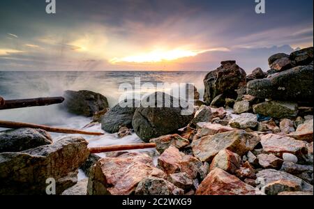 L'eau de l'océan des vagues sur la plage de rock avec beau coucher de soleil Ciel et nuages. Éclaboussures des vagues de la mer sur la pierre en mer sur la côte de l'été. Nature Paysage. Scieries Banque D'Images