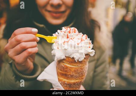 Trdelnik ou Trdlo avec de la crème dans les mains d'une belle fille d'hiver en République tchèque, Prague au marché de Noël Banque D'Images