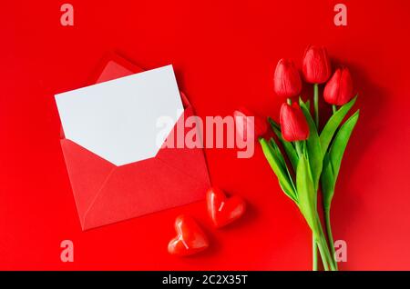 Carte de vœux avec amour. Enveloppe rouge avec papier blanc, bouquet de tulipes et bougies en forme de coeur. Vue de dessus avec espace pour votre texte. Pose plate Banque D'Images