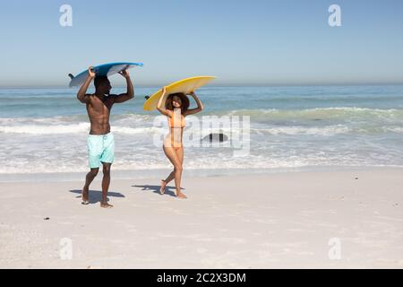 Couple mixte de course tenant des planches de surf sur la plage Banque D'Images