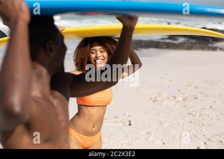 Couple mixte de course tenant des planches de surf sur la plage Banque D'Images