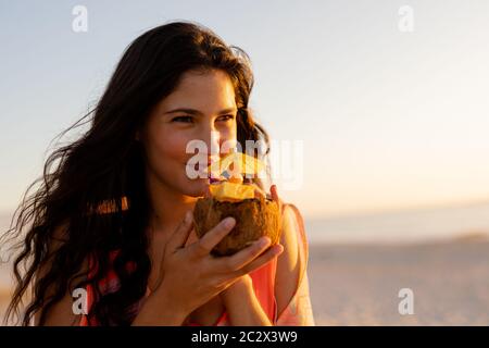 Jeune femme de race mixte qui boit un cocktail sur la plage Banque D'Images